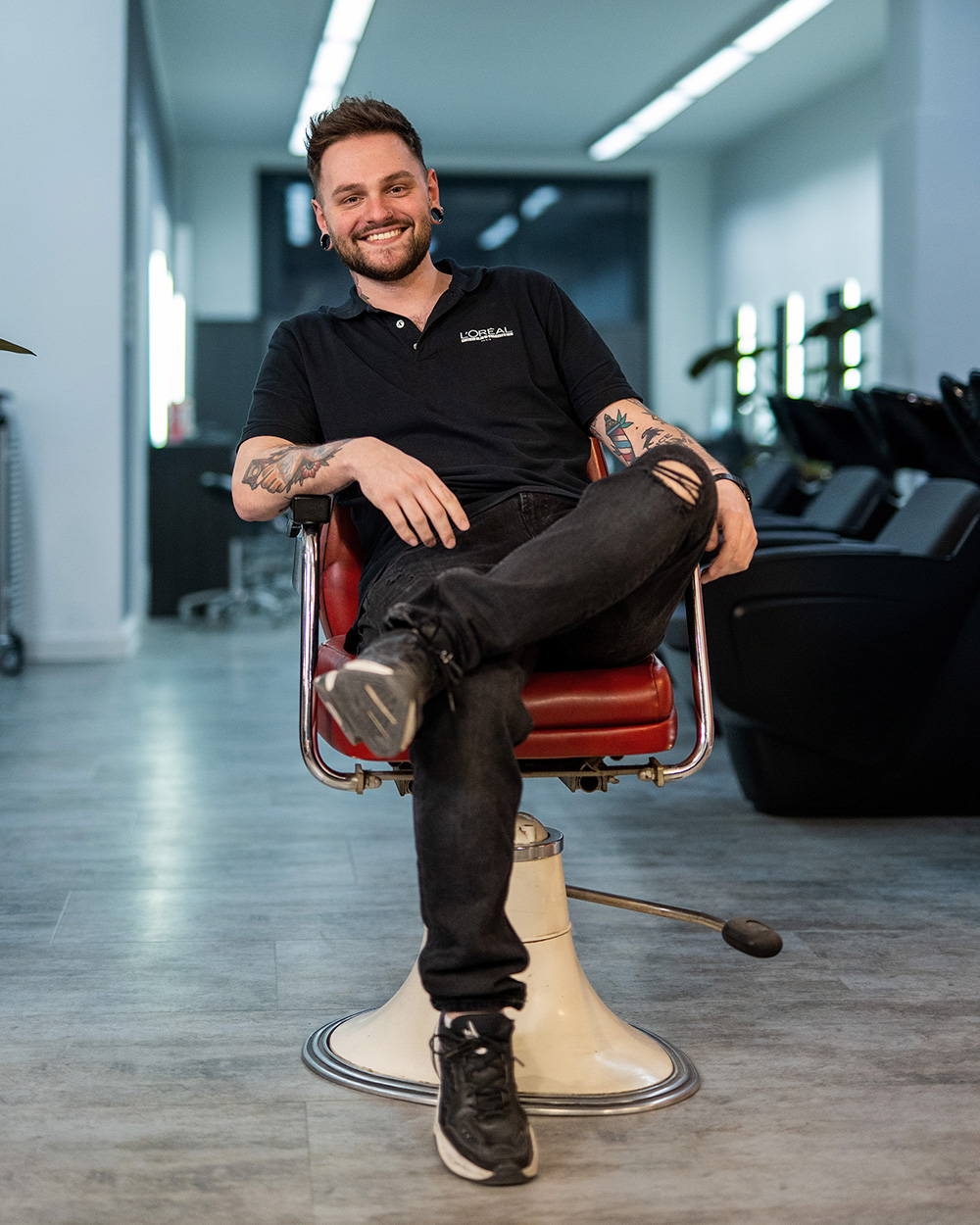 Frisör sitzt entspannt in einem roten Stuhl in einem modernen Salon.