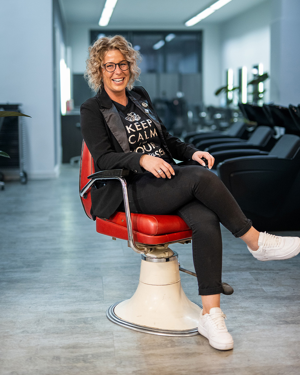 Lächelnde Frau in einem Friseurstuhl, leger gekleidet, mit einem humorvollen T-Shirt.
